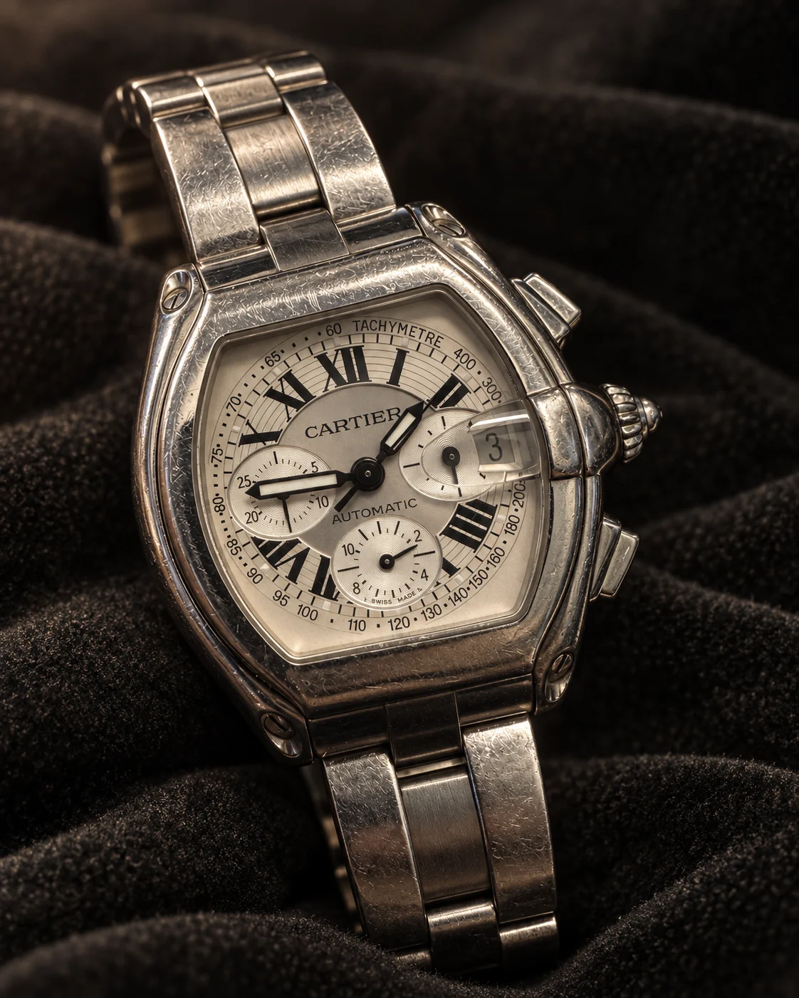 A stainless steel Cartier Roadster Chronograph XL with a silver Roman dial, on its steel bracelet, resting on dark fabric